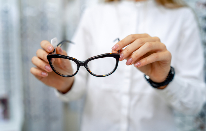 optometrist in white coat holding a pair of cat eye glasses