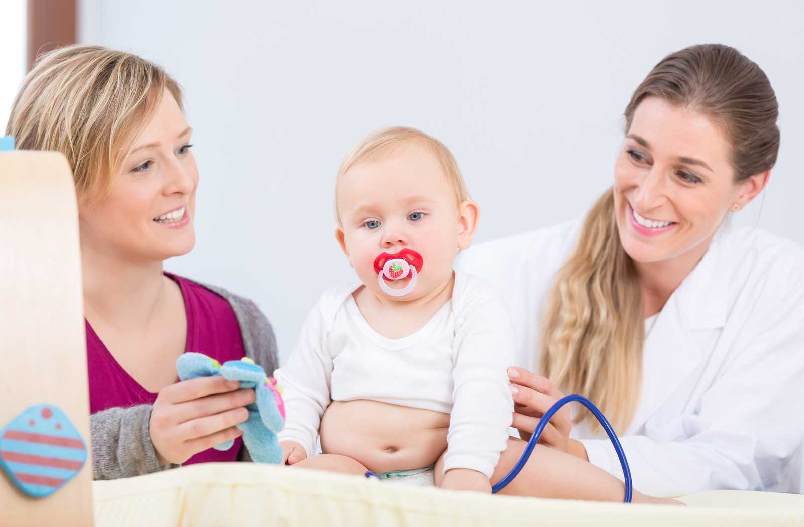 mother with baby helping optometrist conduct first eye exam on white background