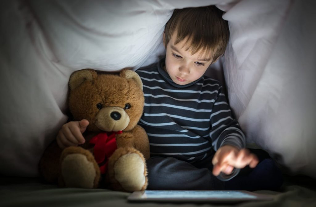A young child uses a tablet in the dark at night when he should be sleeping