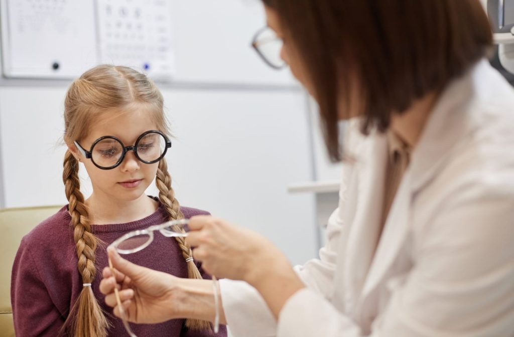 Optometrist helping a little girl fit glasses correctly