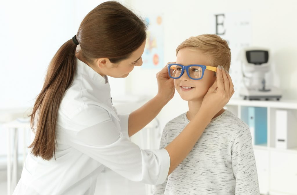 A female optometrist fitting a young boy with a pair of glasses