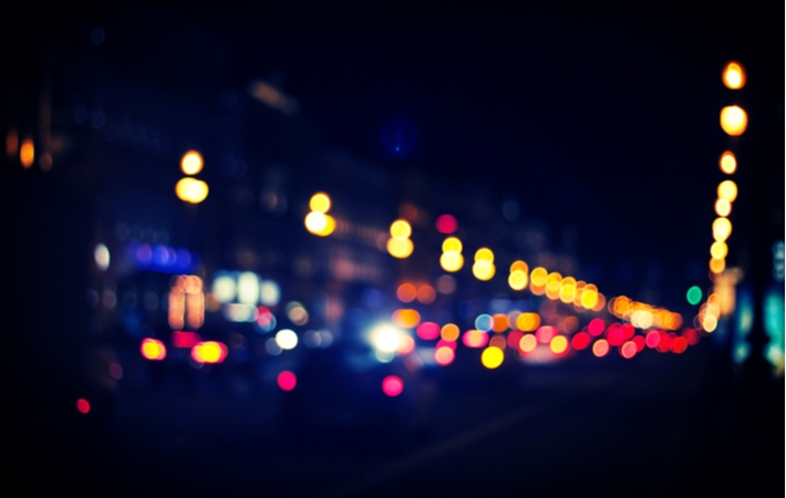 An extremely blurry view of a busy street at night, mostly seeing the break lights of cars in the distance