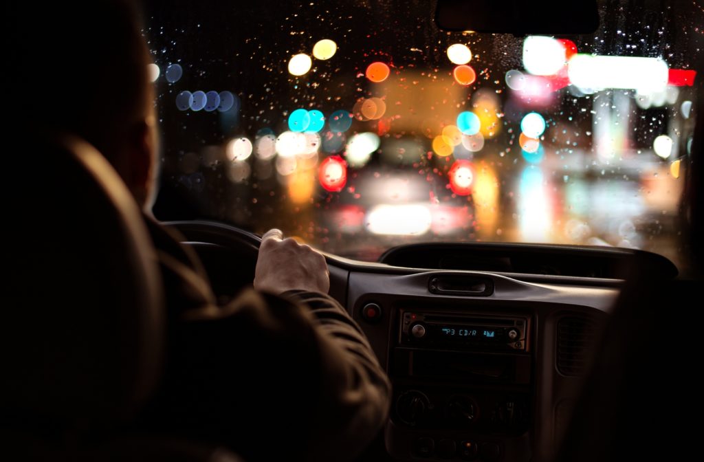 An over the shoulder view of someone driving at night, with the car in front blurred