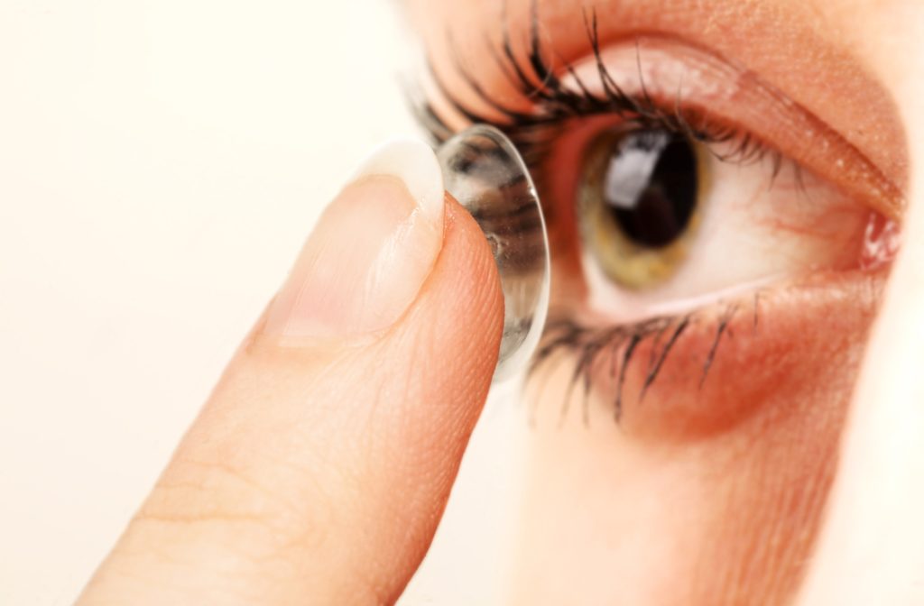 A close-up of a contact lens resting on a woman's fingertip as she puts it in her eye
