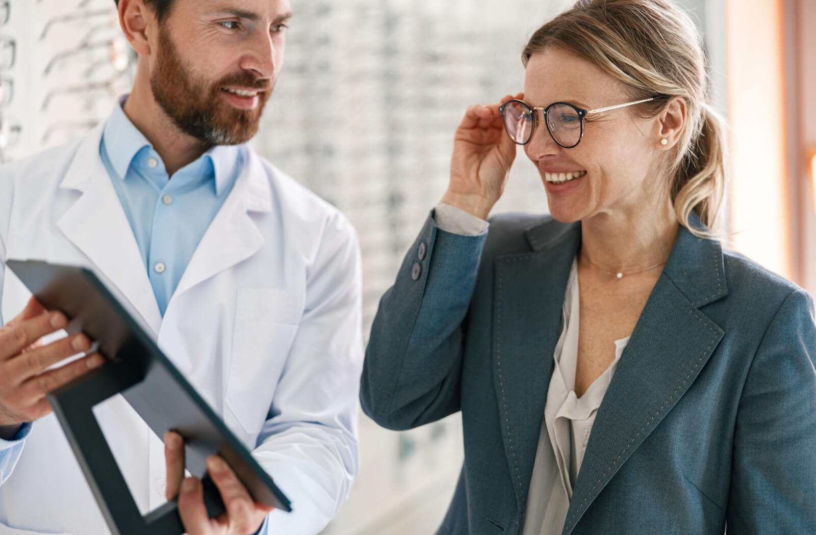 A male optometrist is helping a woman to choose glasses in an optical store.