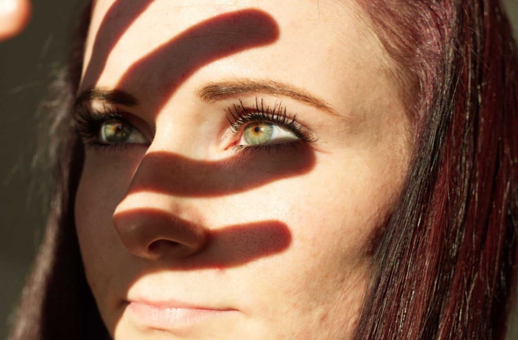 A woman with light blue-green eyes using her hand to block the sunlight from her eyes