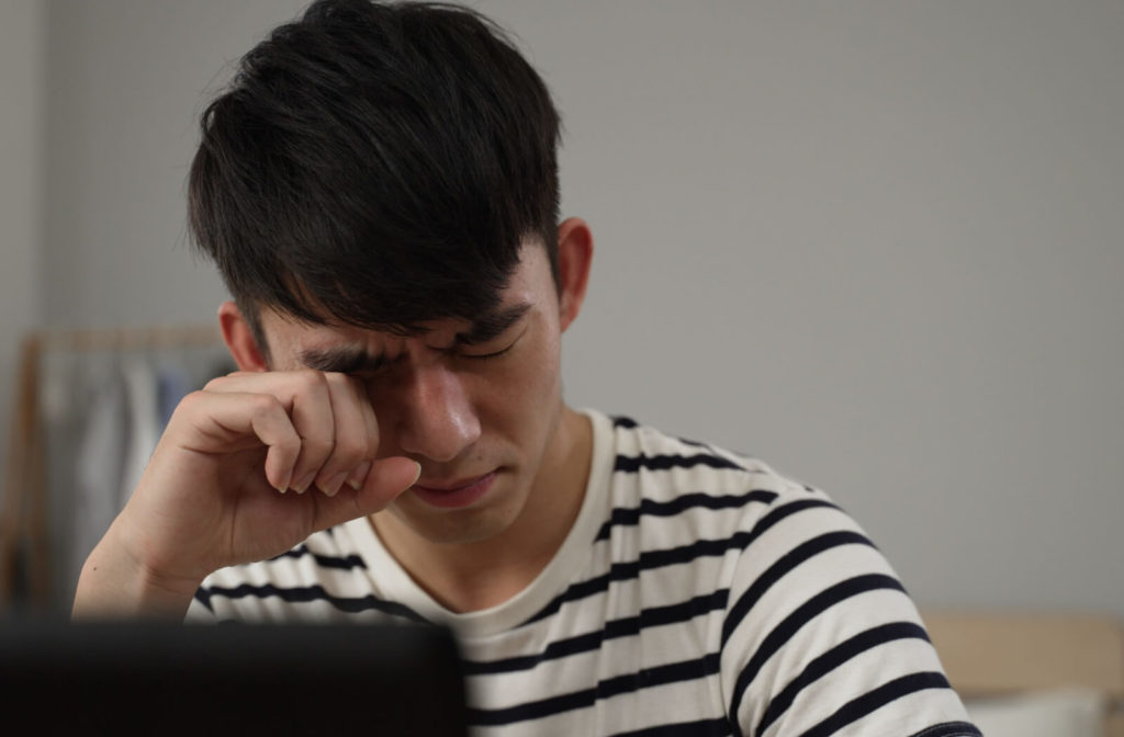 A man rubbing his right eyelid with his right hand due to eye pain.