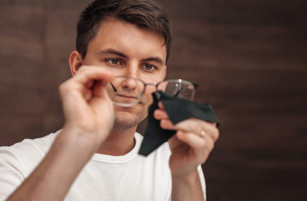 A man in a white shirt cleaning his glasses using a black microfibre cloth