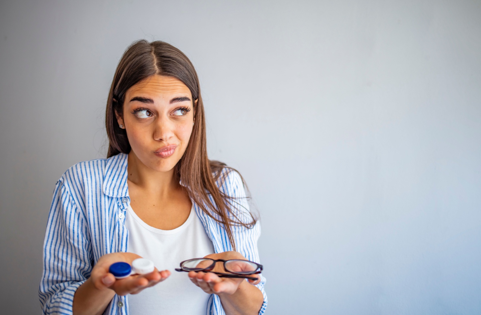 A woman holding a contact lens container on her right hand and an eyeglass on her left hand
