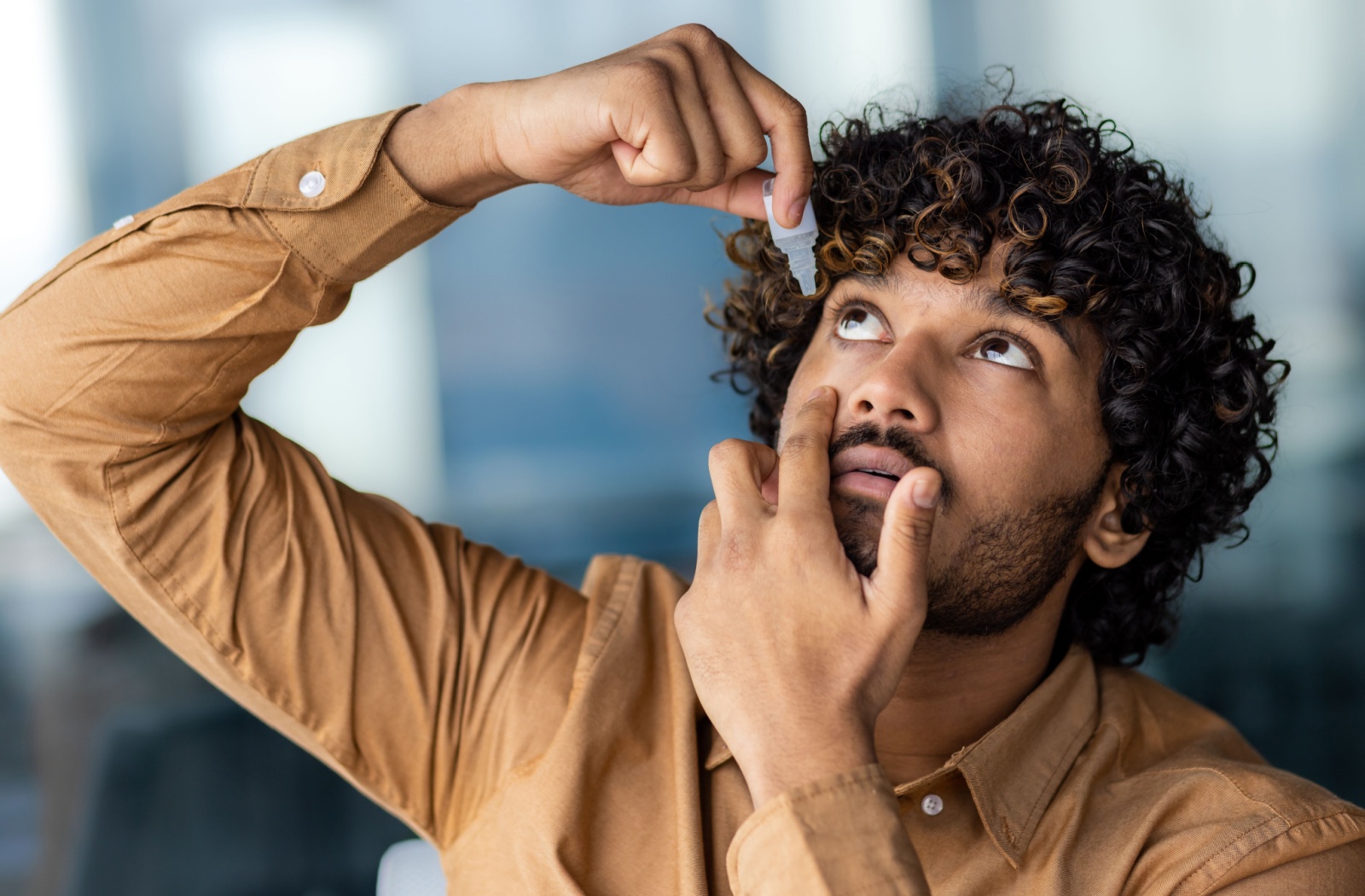 A man putting eye drops into his eye.