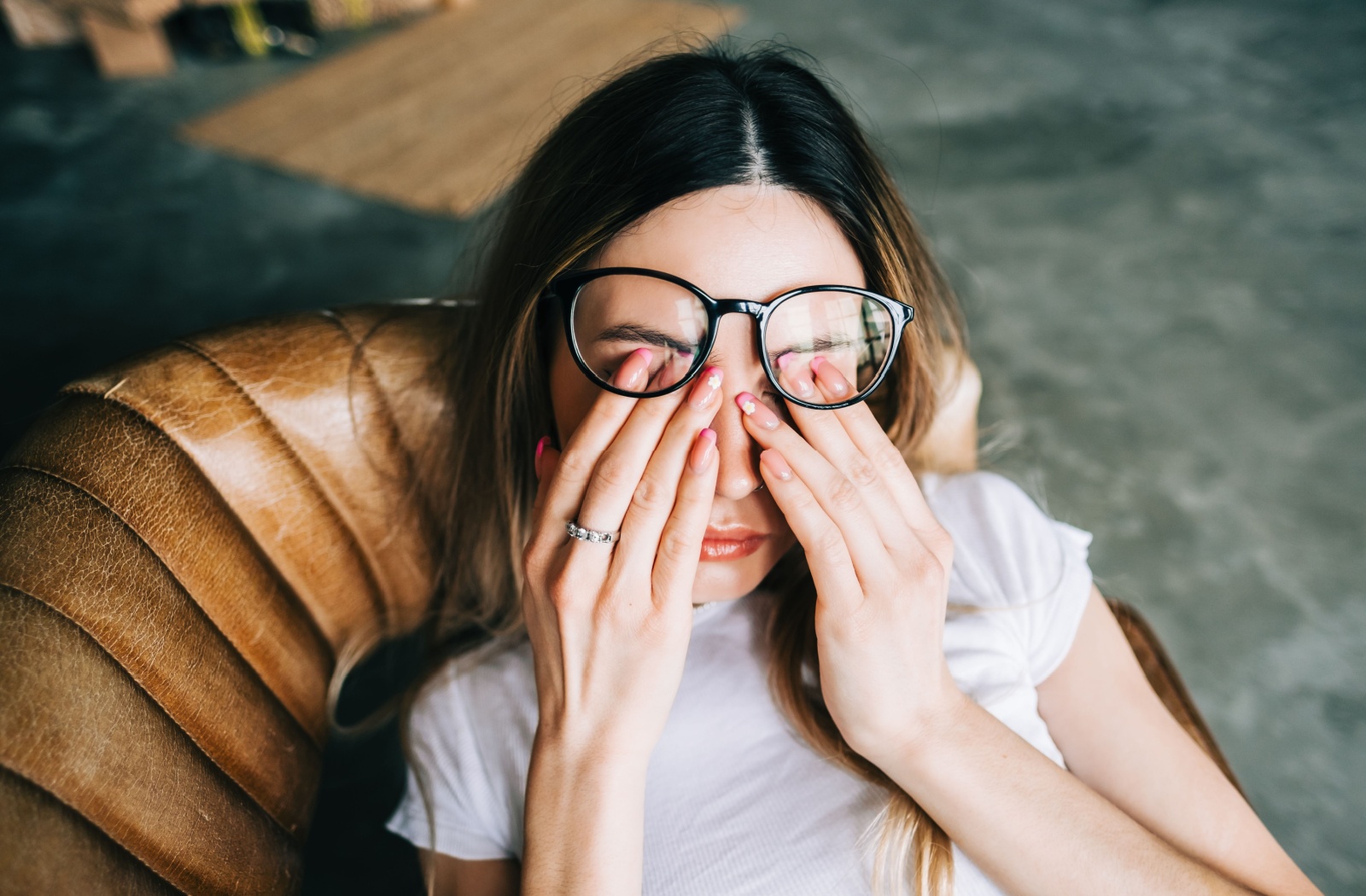 A person with pink fingernail tips pushes their glasses up to rub their eyes from a headache