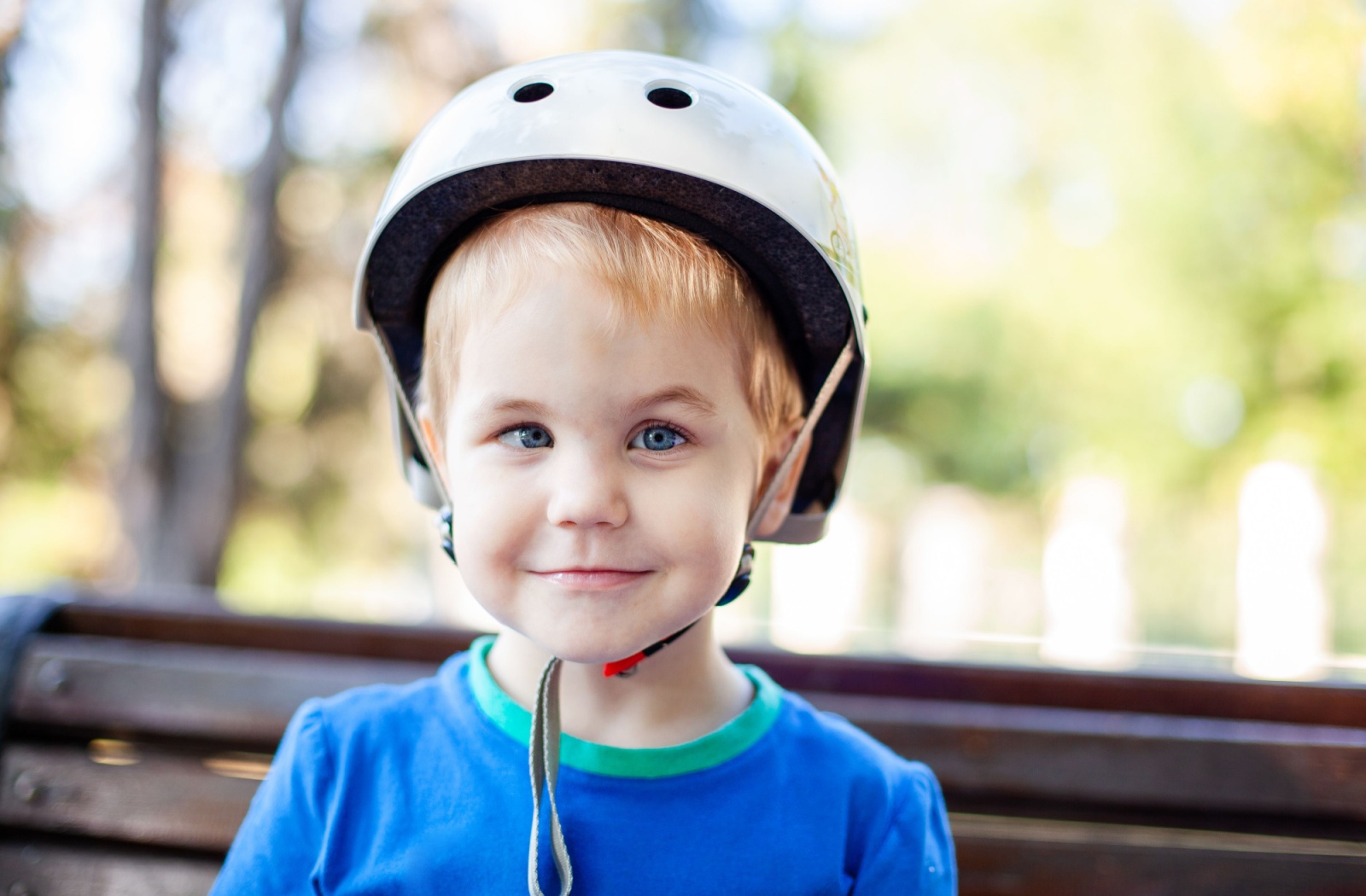 A child standing outside smiles and displays a turned eye or strabismus.
