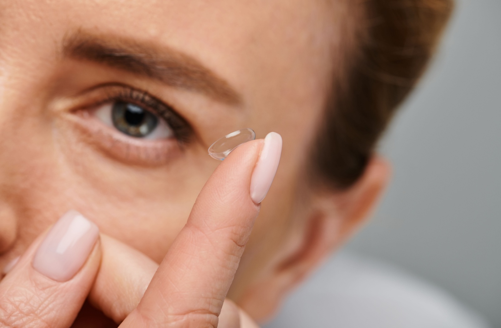 A close-up of a person holding a contact lens on their index finger, ready to place it in their left eye.