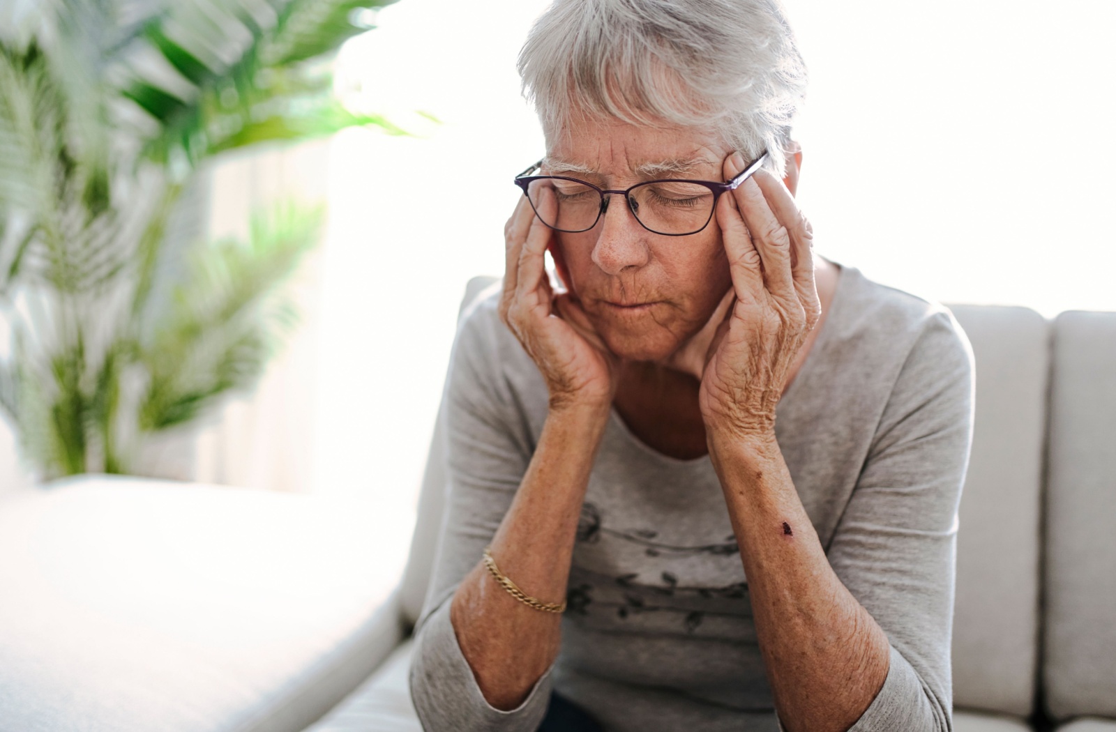 An older adult with a tension headache due to eye strain rubs their temples gingerly while squinting their eyes closed.
