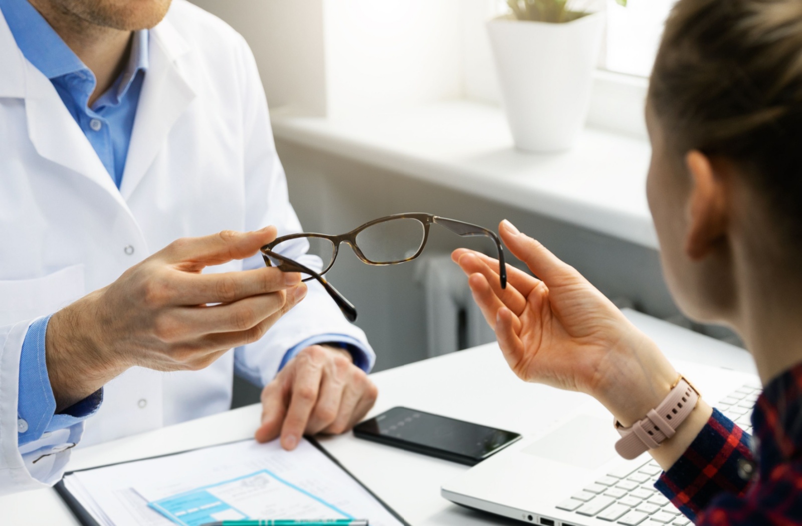 An optometrist handing a patient a new pair of eyeglasses with an updated prescription.