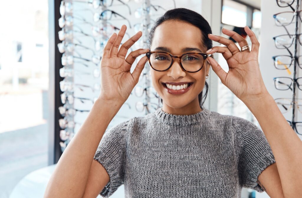 A patient in front of a glasses display wall trying on their new glasses and smiling after an eye exam.
