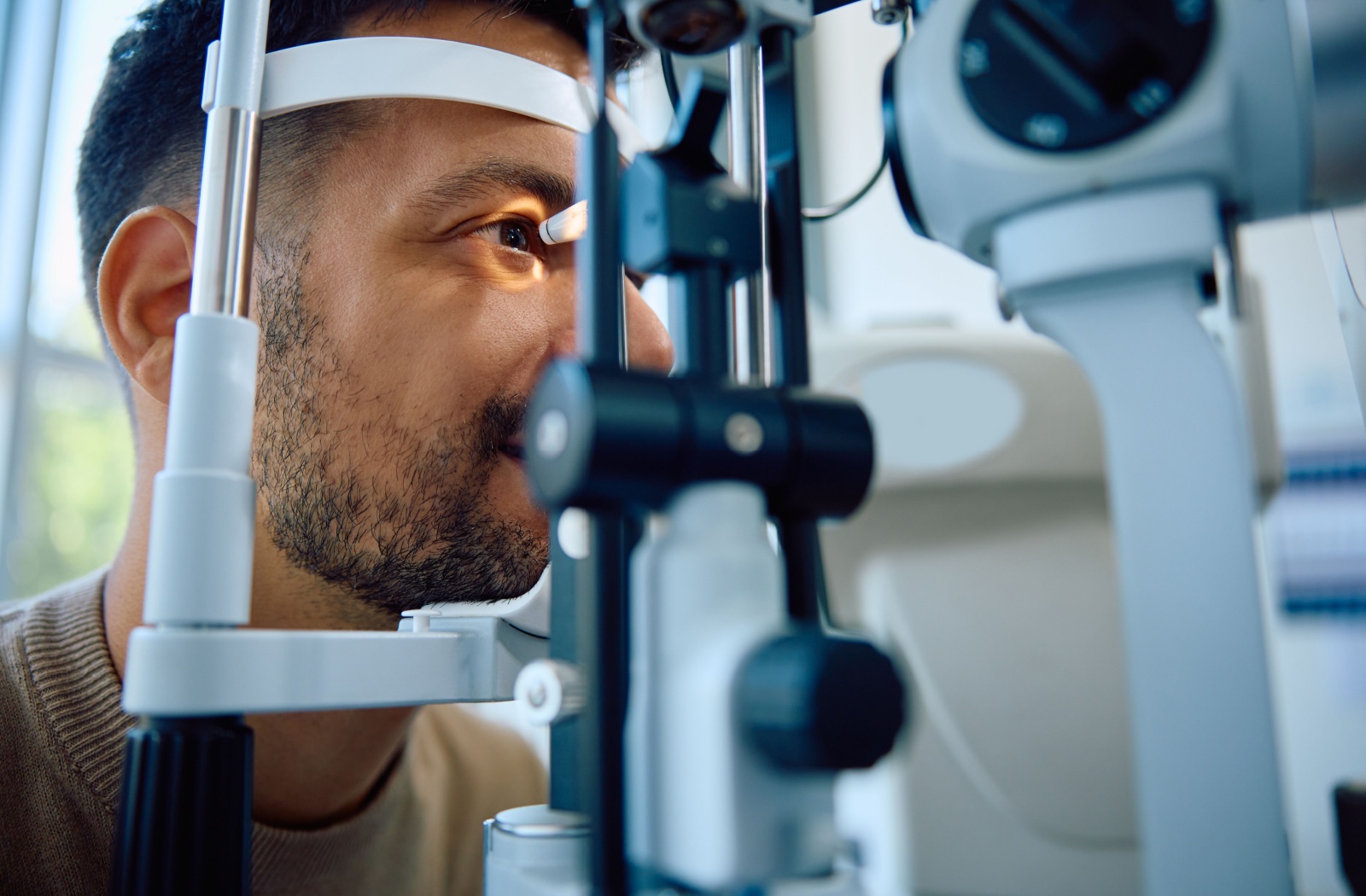 Man receiving an eye exam using a slit lamp at an optometrist’s office.