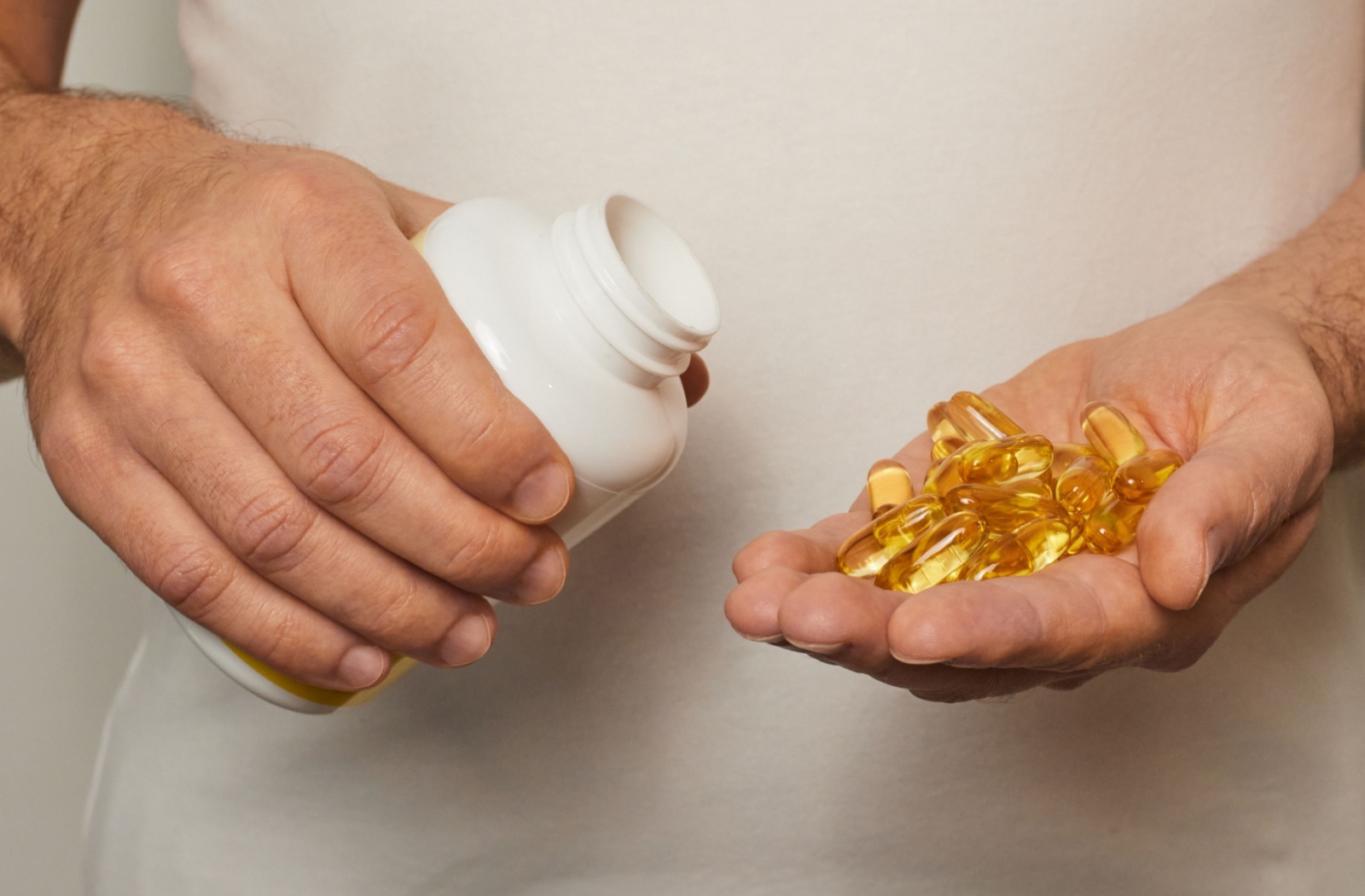 A hand holding a bottle of omega 3 supplements and the other hand holding a handful of omega 3 pills
