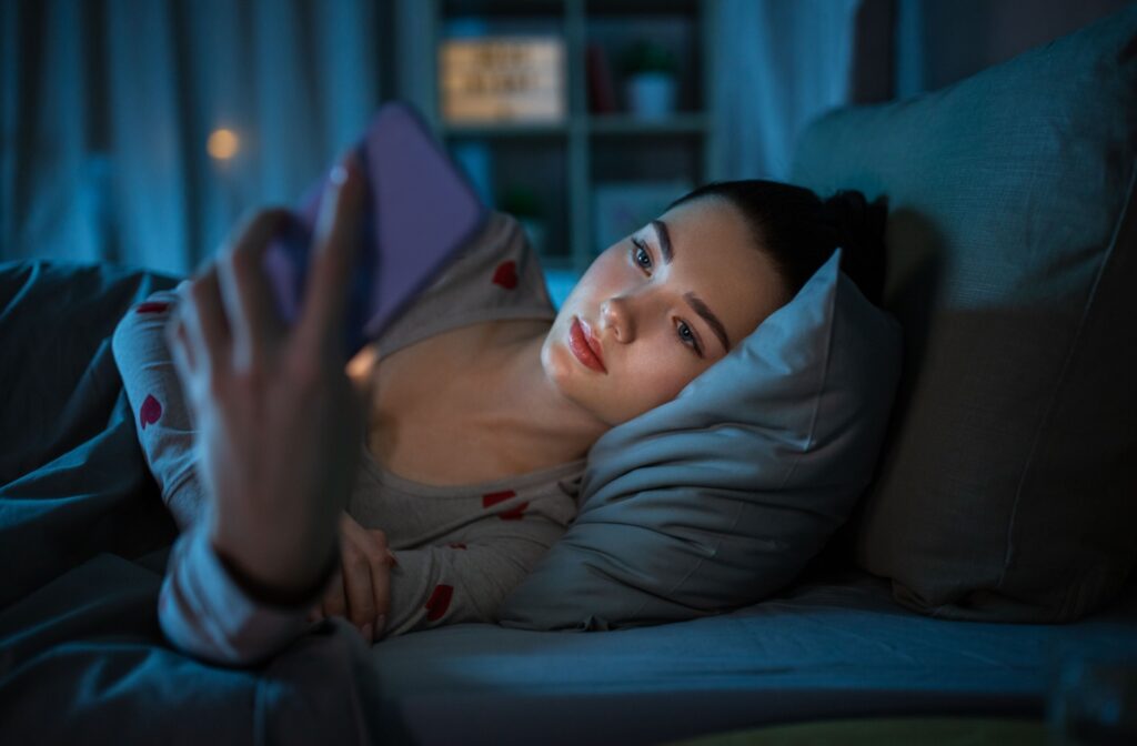 A person laying in bed at night with their phone screen lighting up their face.