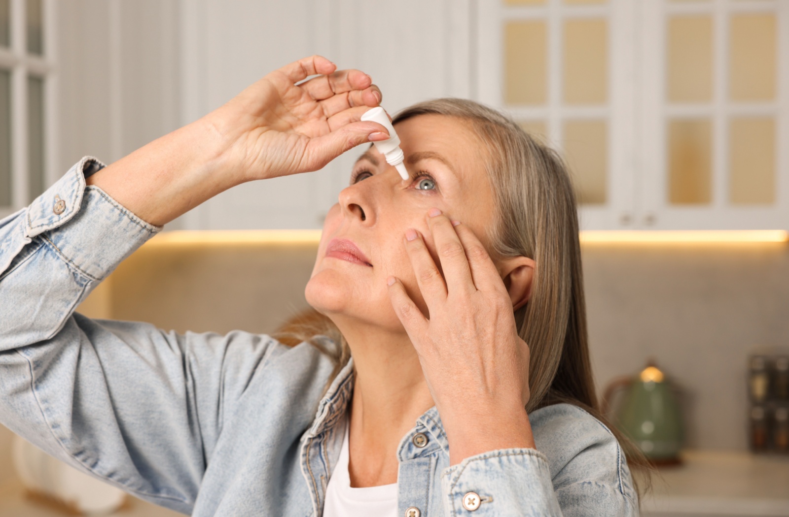 A senior person looks up while they put eye drops in their eye